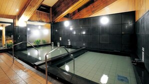 A modern indoor swimming pool with a wooden ceiling and black tiled walls. - Tawarayama Machigoto Ryokan (Nagato)