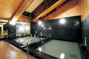 A modern indoor swimming pool with a wooden ceiling and black tiled walls. - Tawarayama Machigoto Ryokan (Nagato)
