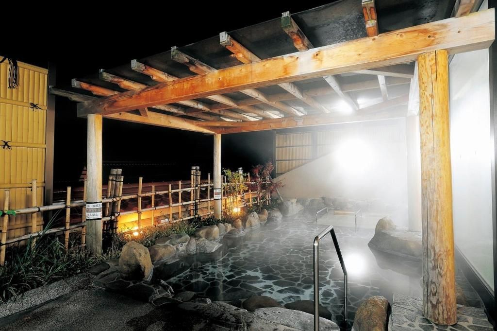 Un onsen japonais traditionnel, avec une structure en bois, un bain en pierre et une atmosphère brumeuse.