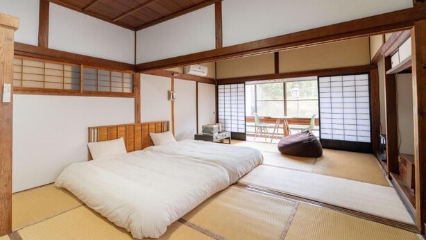 A traditional Japanese-style room with tatami flooring, a bed with white bedding, and a sliding door leading to a balcony. - Tawarayama Machigoto Ryokan (Nagato)