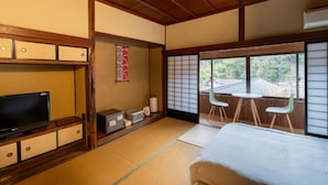 A traditional Japanese room with tatami flooring, a television, a futon bed, and a sliding door leading to an outdoor area with a view of the surrounding landscape. - Tawarayama Machigoto Ryokan (Nagato)