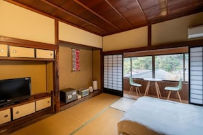 A traditional Japanese room with tatami flooring, a television, a futon bed, and a sliding door leading to an outdoor area with a view of the surrounding landscape. - Tawarayama Machigoto Ryokan (Nagato)