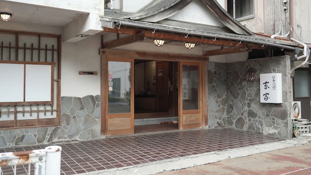 Un edificio japonés tradicional con un acceso de tejas, puertas de madera y un muro de piedra.