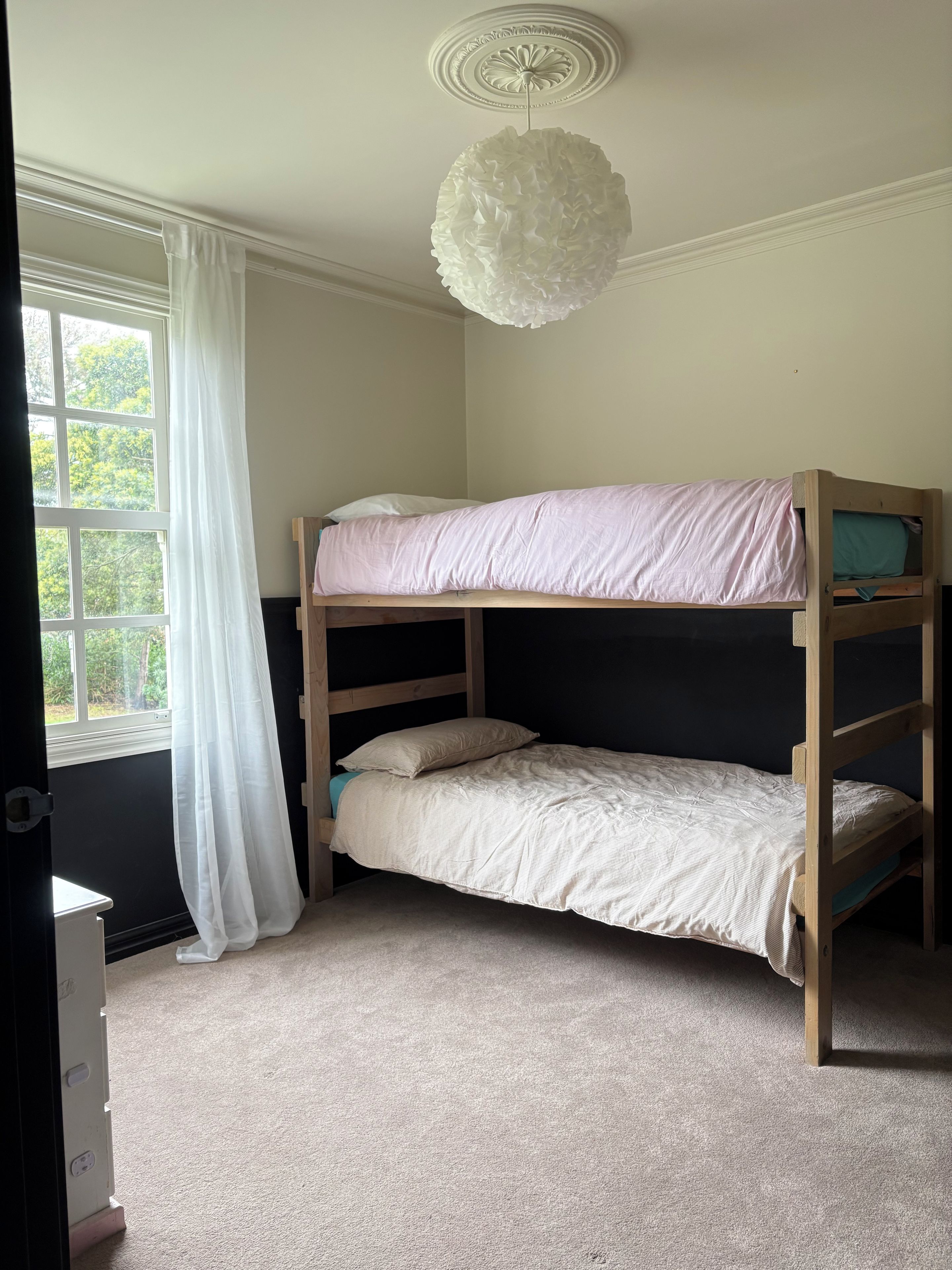 A bunk bed room with a window, white curtains, and a ceiling light fixture.