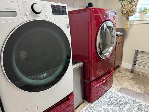 A compact laundry area with a front-loading white washer and a red stacked washer-dryer unit.