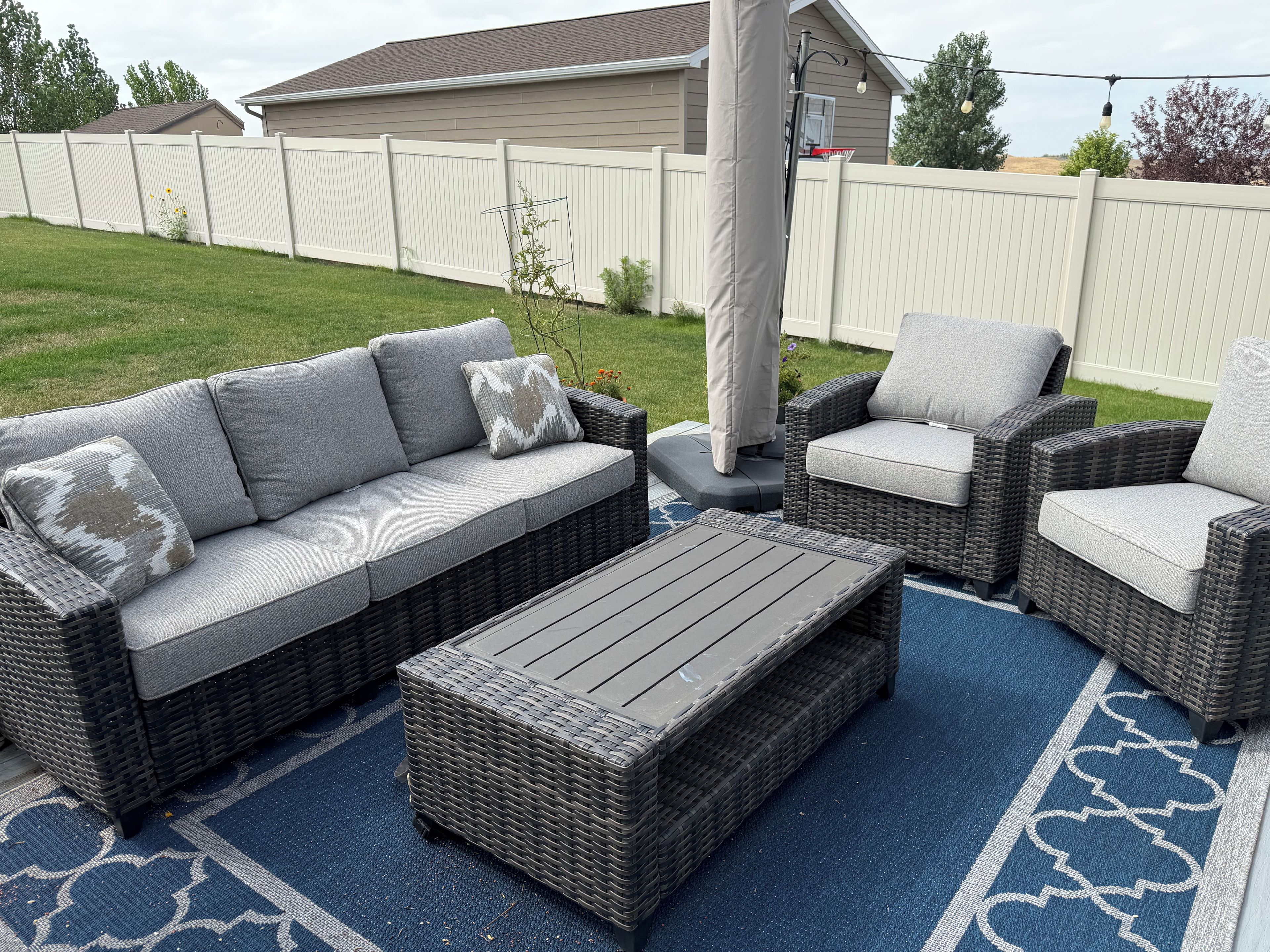 Un patio con un sofá gris, dos sillones y una mesita baja, todo sobre una alfombra con estampado azul.