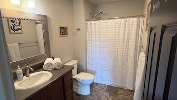 A bathroom with a double sink, toilet, and shower curtain.