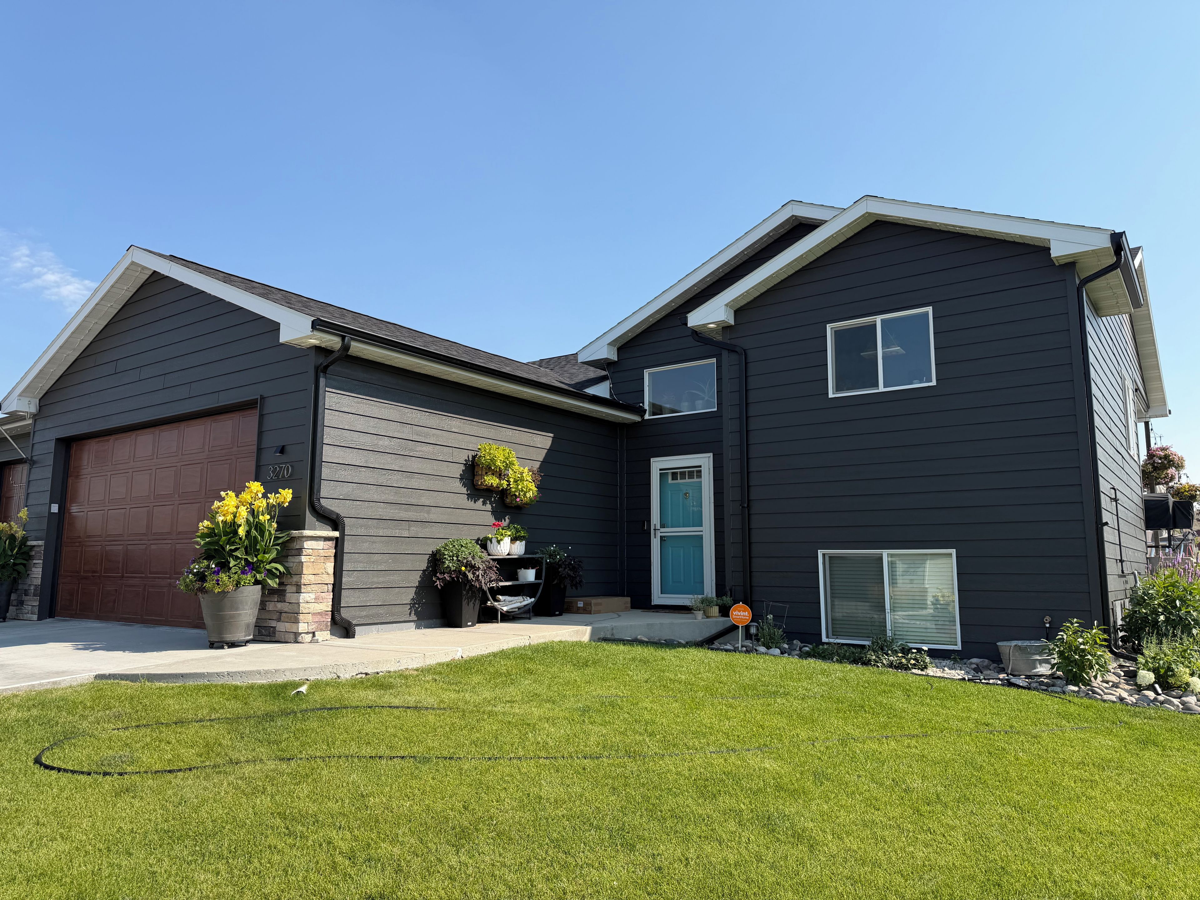 A two-story house with a dark exterior, a garage, and a well-maintained lawn.