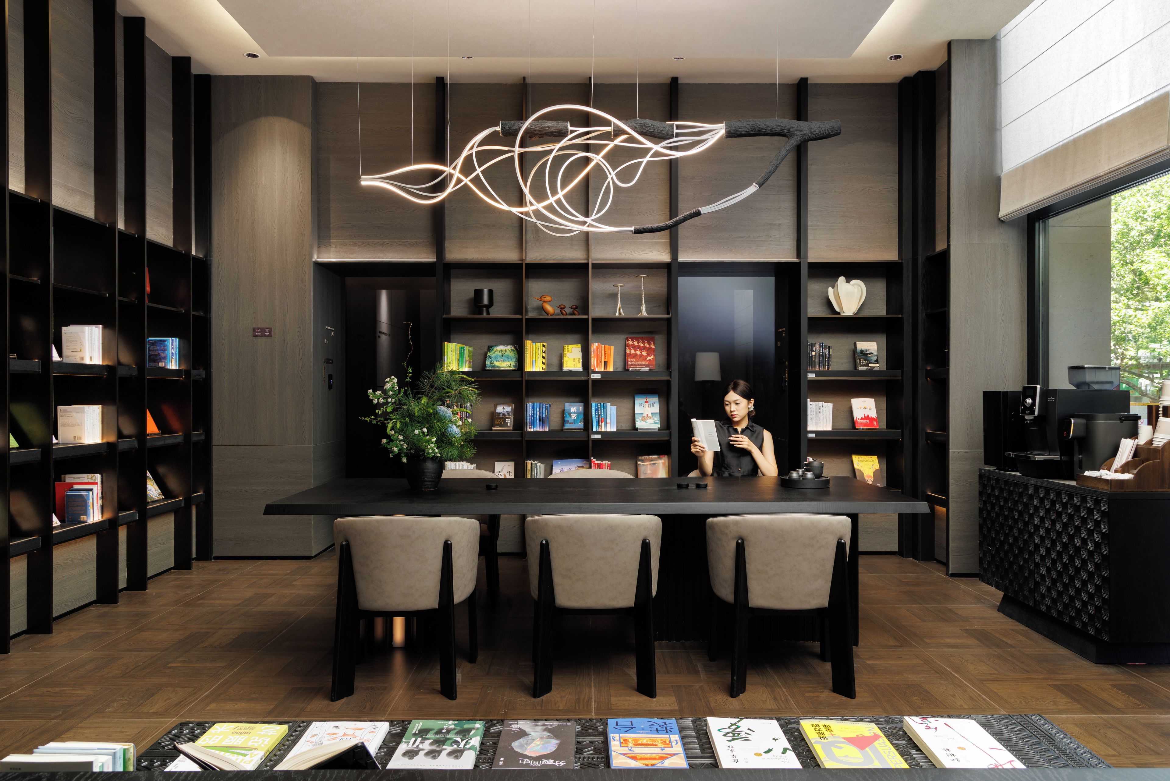 Eine moderne Bibliothek mit Bücherregalen, einem zentralen Tisch und Stühlen.