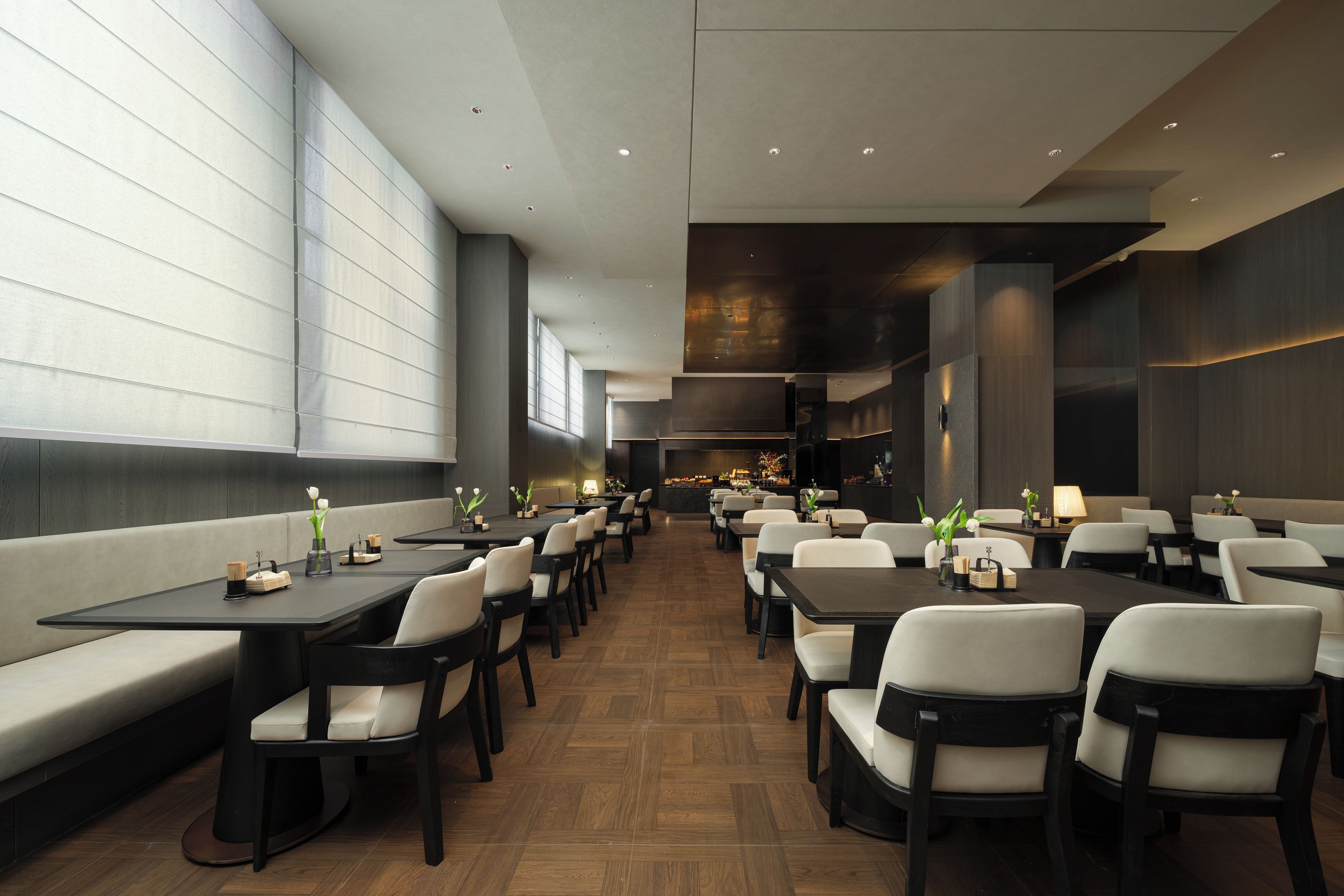 Um restaurante moderno com mesas compridas e cabines, piso de madeira e janelas amplas.