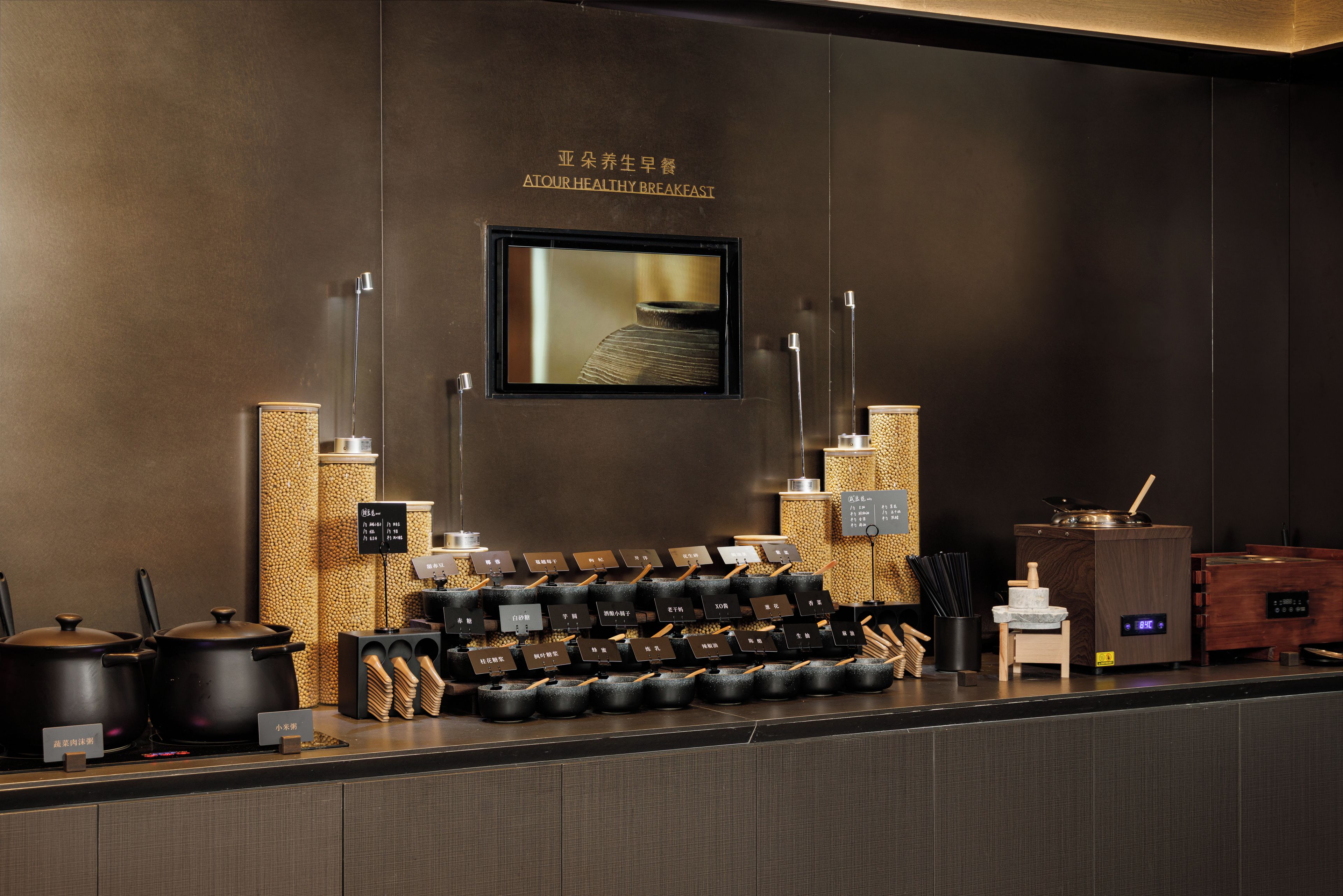 A breakfast bar with a variety of dishes and utensils, a wall-mounted television, and a wooden textured wall.