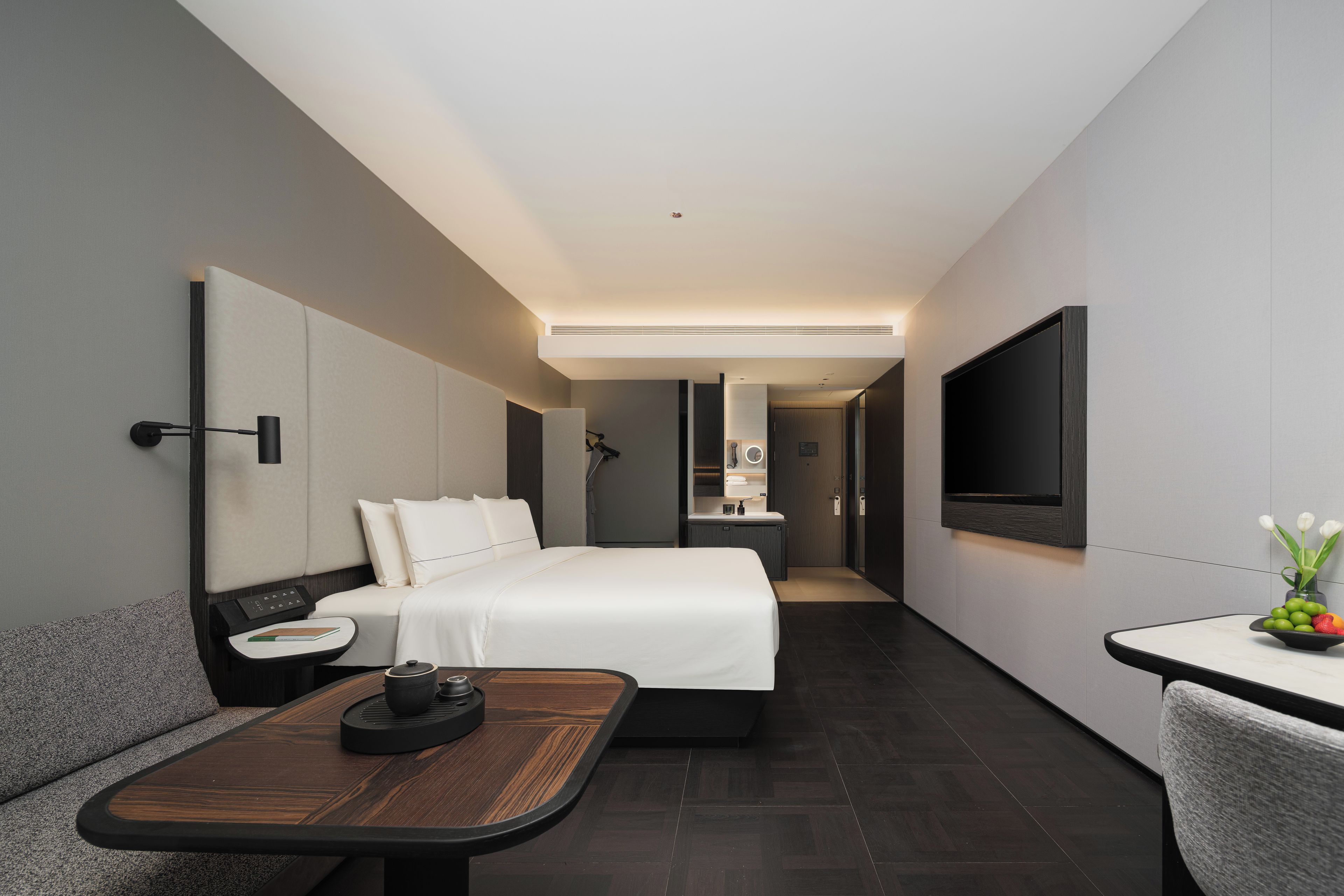 A modern hotel room with a bed, bedside table, and a TV mounted on the wall.
