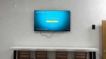 A flat-screen TV mounted on a wall above a white marble-topped table with four wooden chairs.