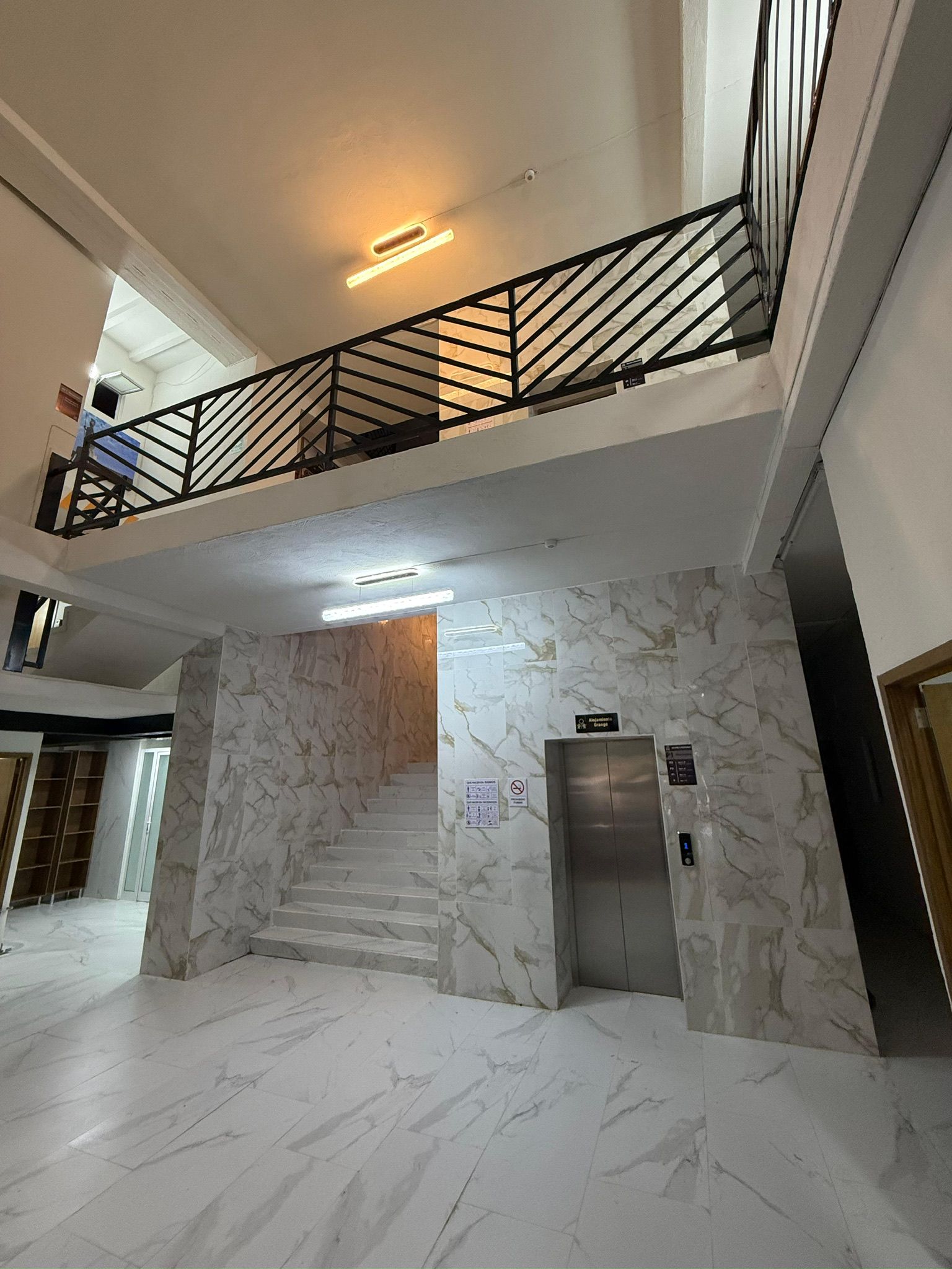 A multi-level interior with marble flooring, a staircase, an elevator, and a balcony with a metal railing.