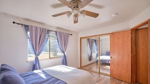 Un dormitorio con cama, cortinas, ventilador de techo y puerta corrediza de vidrio que da a otra habitación.