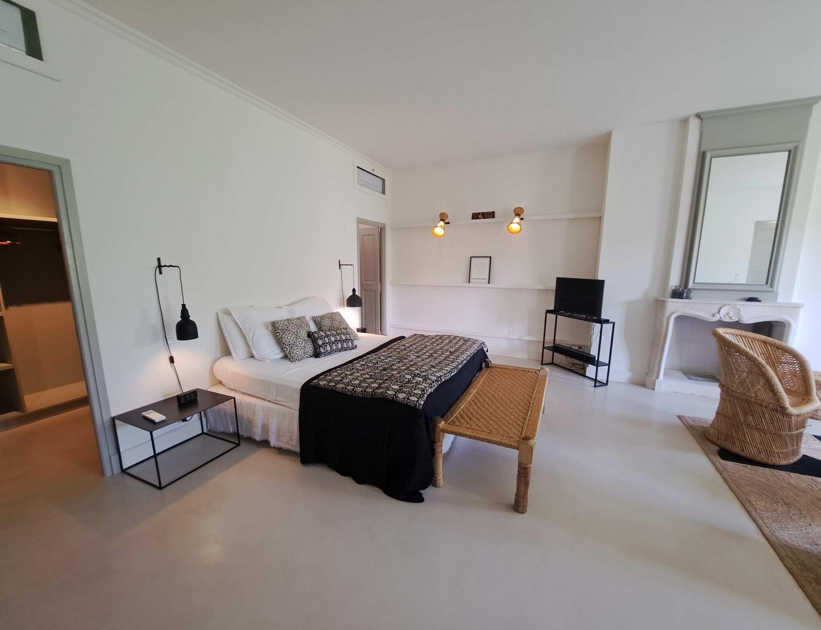 A modern bedroom with a bed, bedside tables, a chair, a television, and a fireplace.