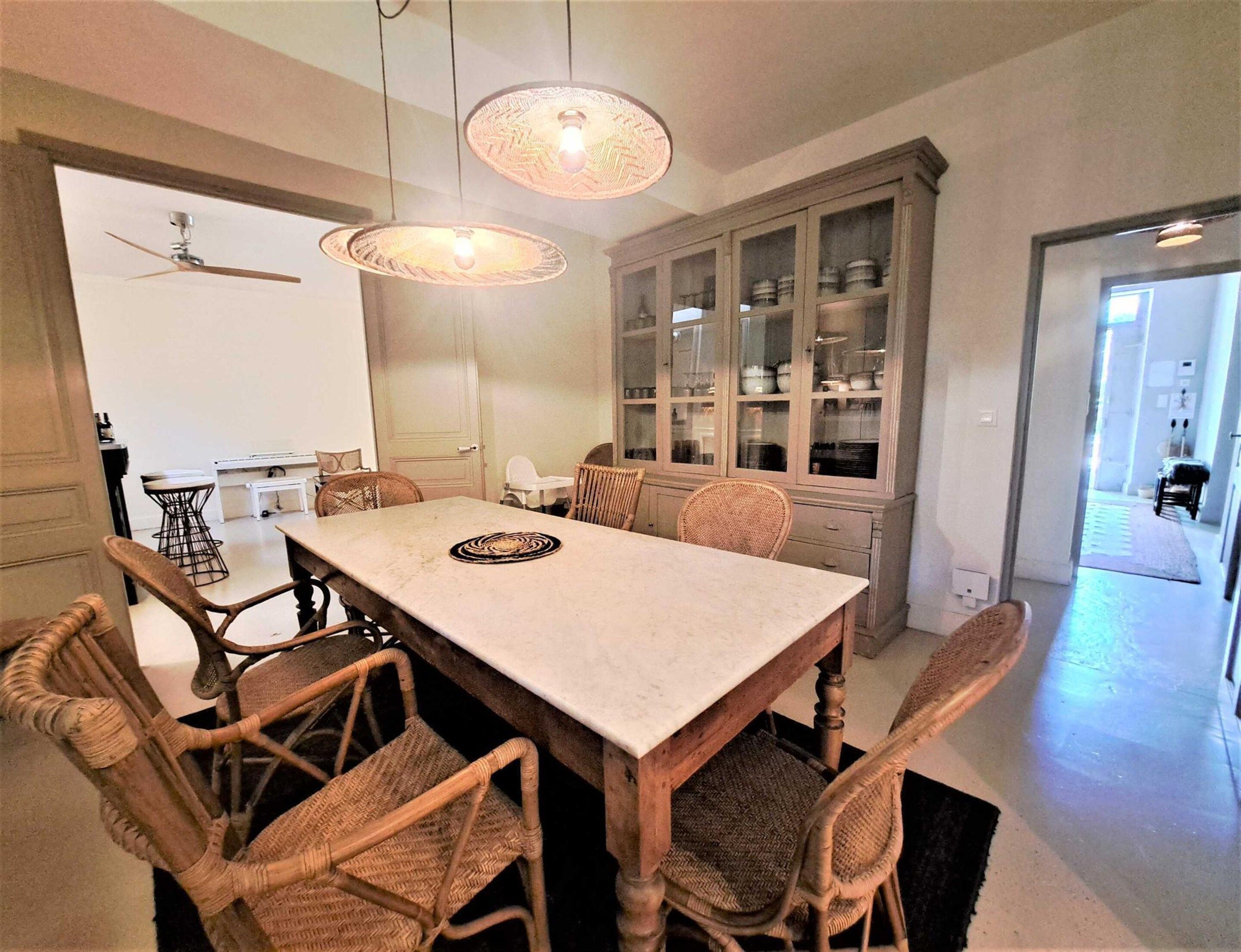 A dining area with a large table, wicker chairs, and a cabinet with glass doors.