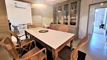 A dining area with a large table, wicker chairs, and a cabinet with glass doors.
