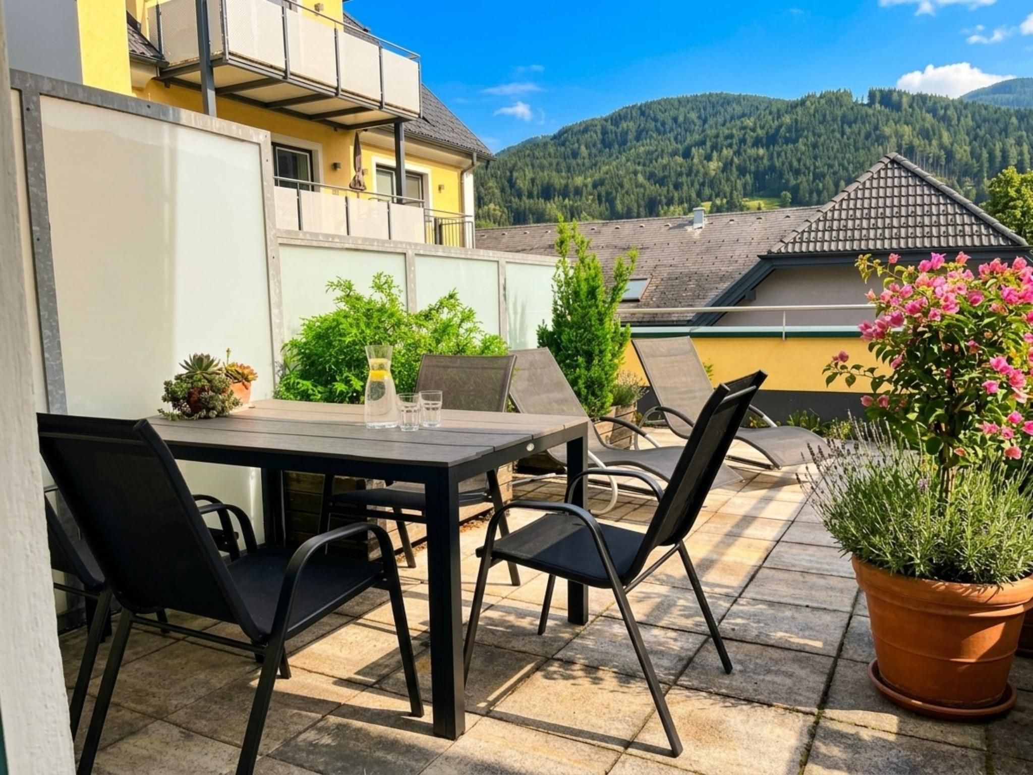 Eine Terrasse im Freien mit Tisch und Stühlen, umgeben von Blumentöpfen und Blick auf einen Berg.