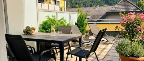 An outdoor patio with a table and chairs, surrounded by potted plants and a view of a mountain.