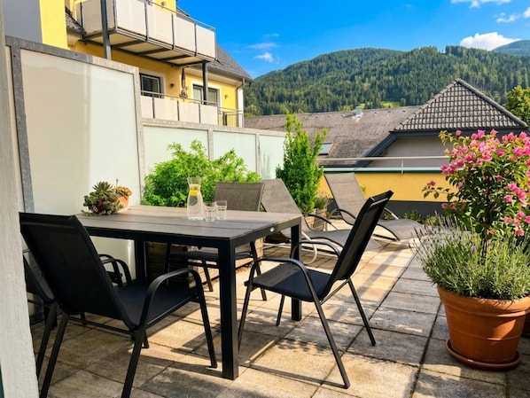 Um pátio externo com mesa e cadeiras, rodeado por vasos de plantas e vista para uma montanha.