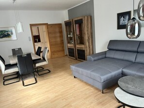 Ein modernes Wohnzimmer mit einem grauen Sofa, einem Esstisch mit Stühlen und einer Holzkommode.