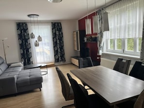 Ein modernes Wohnzimmer mit einem grauen Sofa, einem Esstisch mit Stühlen und einer Küchenzeile mit einem roten Schrank.