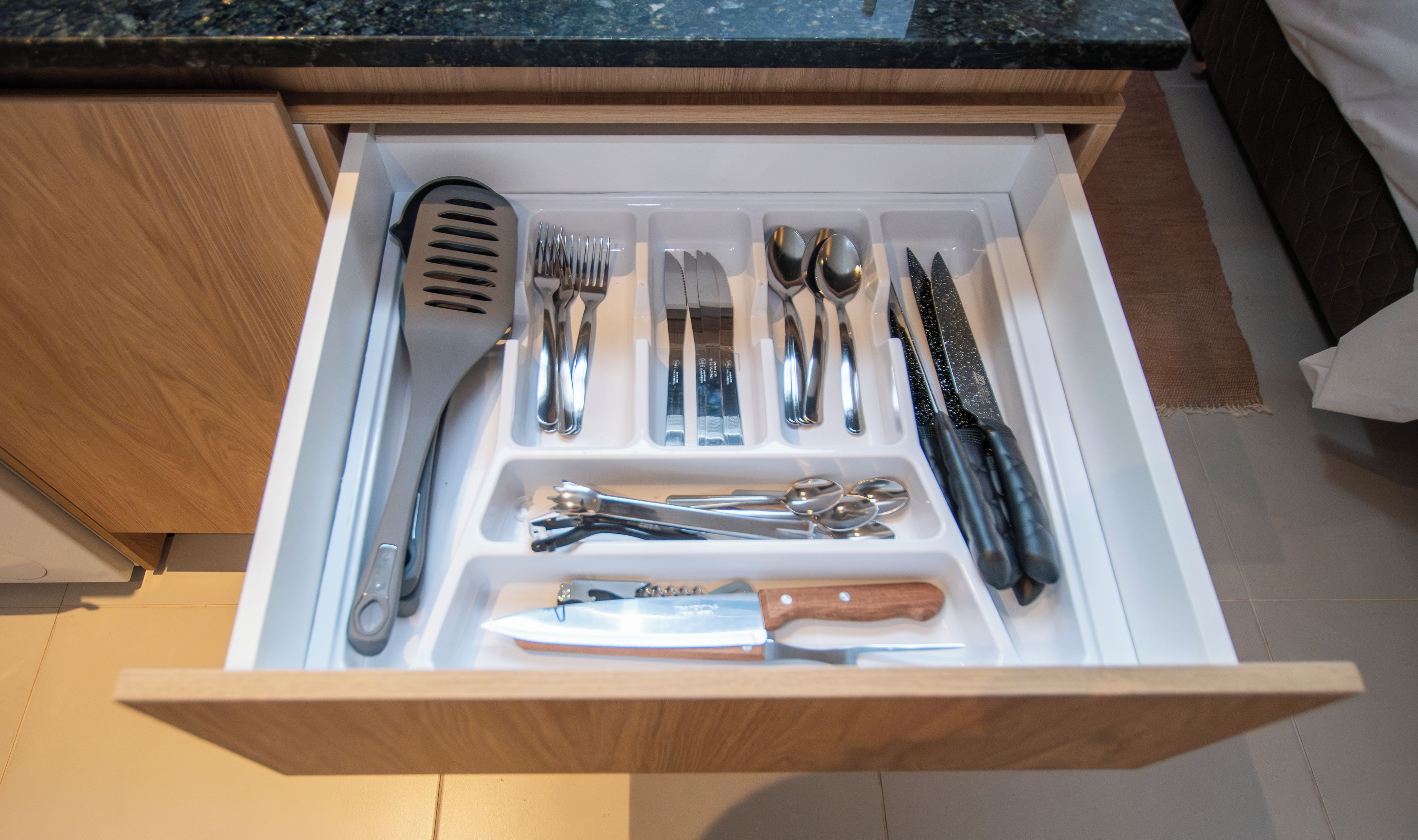 Un cajón con varios utensilios de cocina, incluyendo tenedores, cucharas, cuchillos y un rallador.