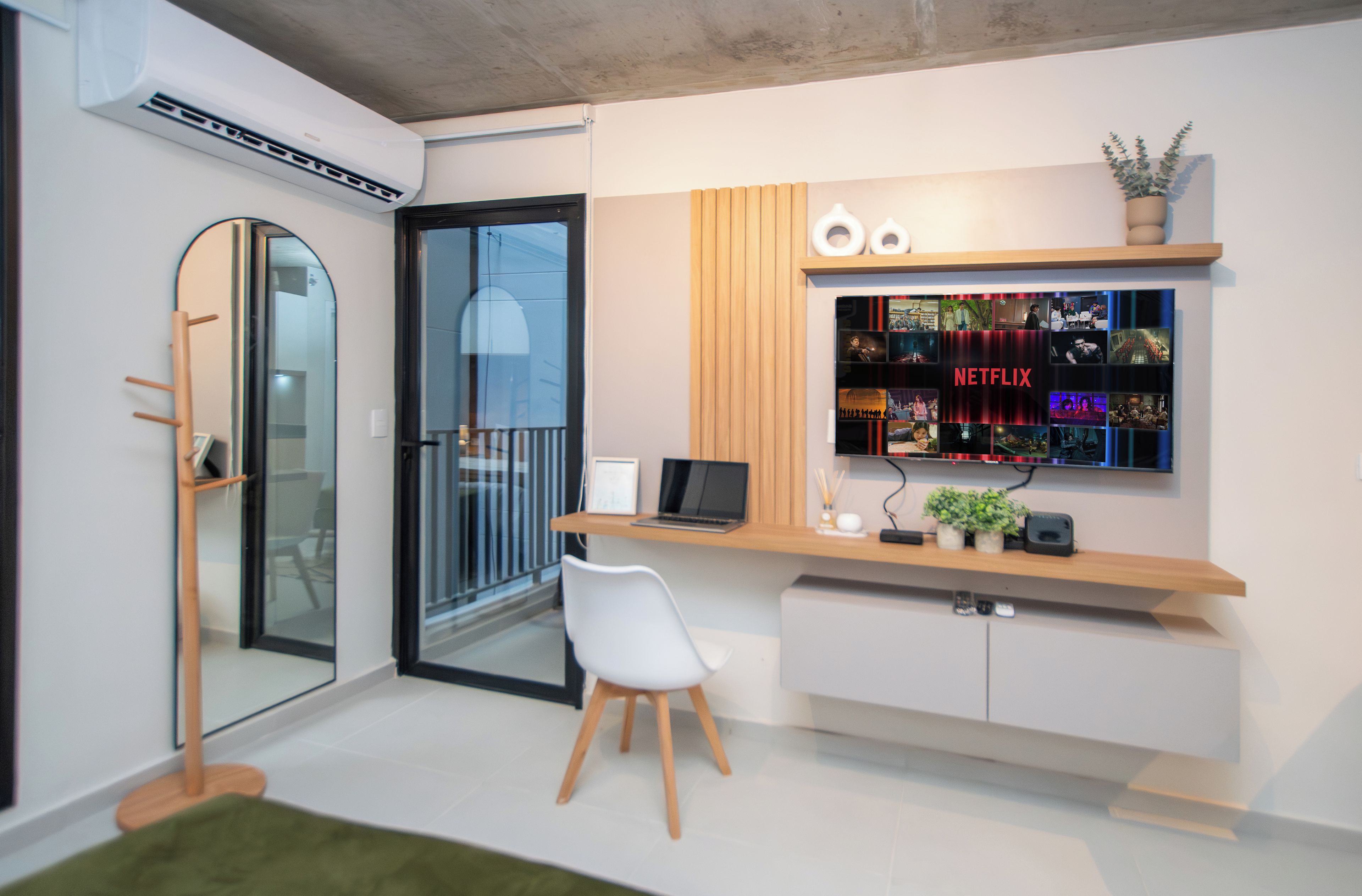A modern office space with a glass door, a desk with a laptop, a white chair, and a wall-mounted shelf with a Netflix sign.