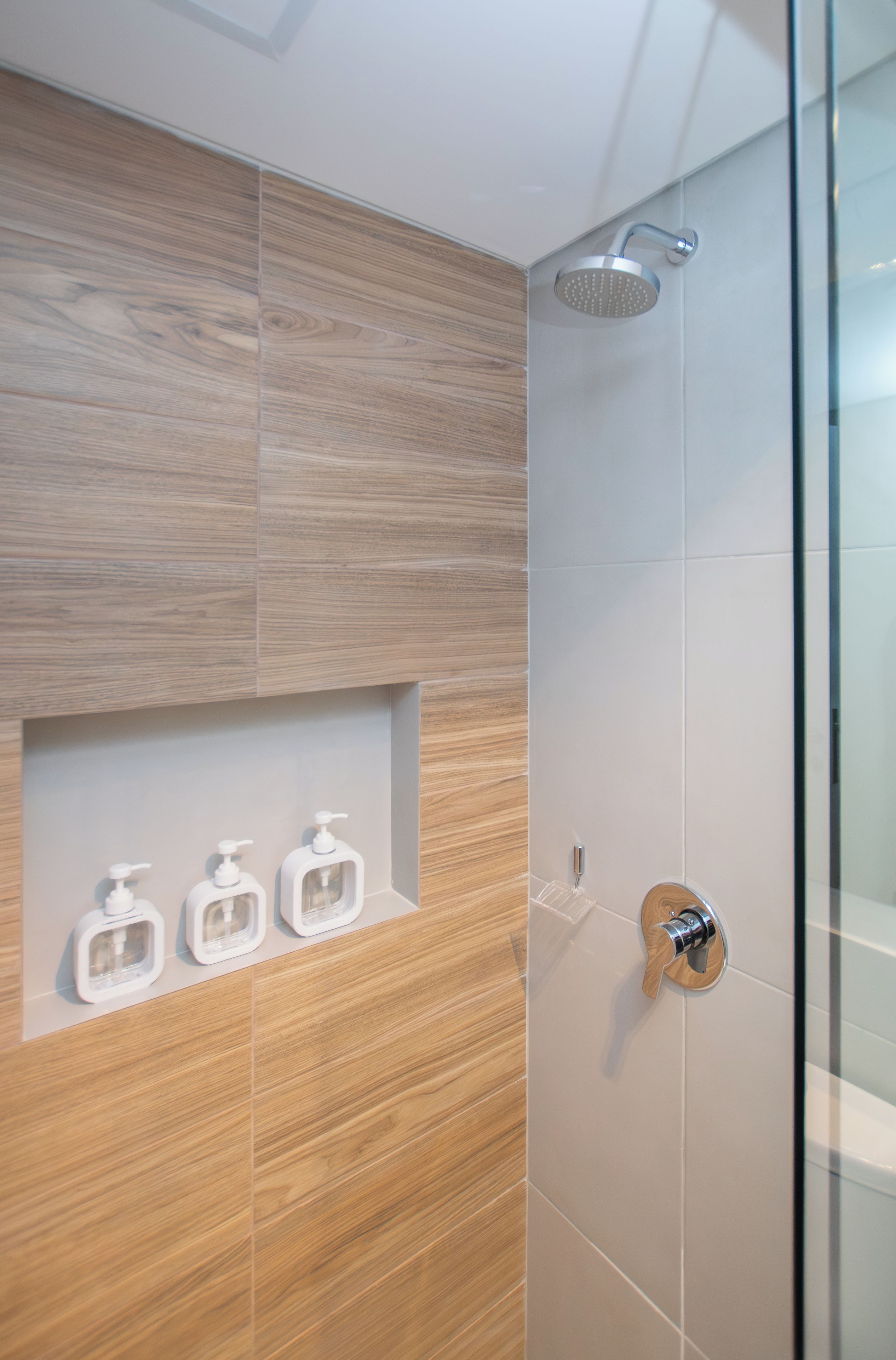 Un baño moderno con ducha, tocador de madera y tres dispensadores de jabón.
