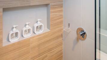 Un baño moderno con ducha, tocador de madera y tres dispensadores de jabón.