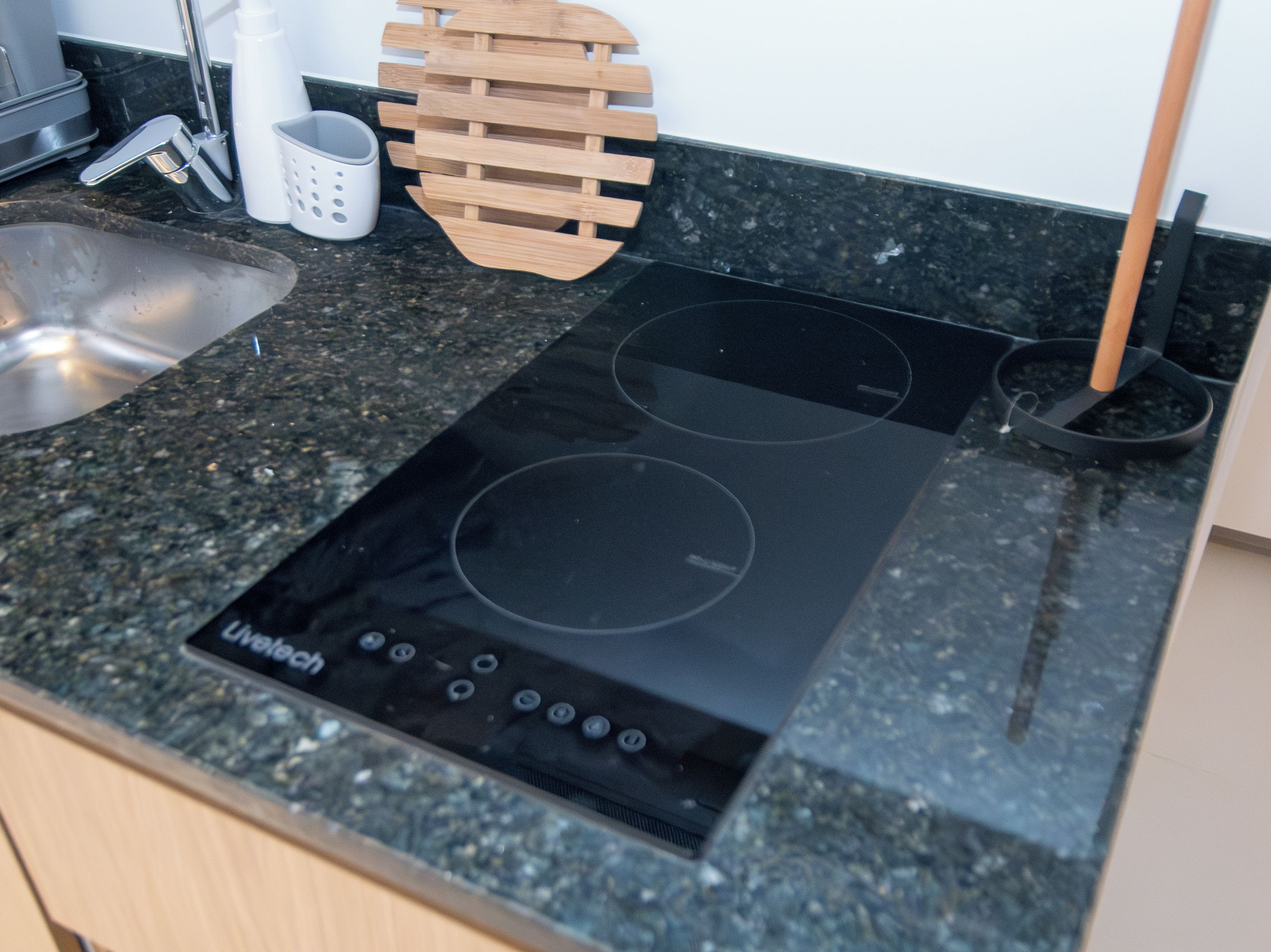 Una cocina con cocina de inducción negra, un lavamanos de acero inoxidable y una tabla de cortar de madera.
