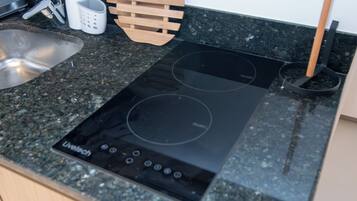 Una cocina con cocina de inducción negra, un lavamanos de acero inoxidable y una tabla de cortar de madera.