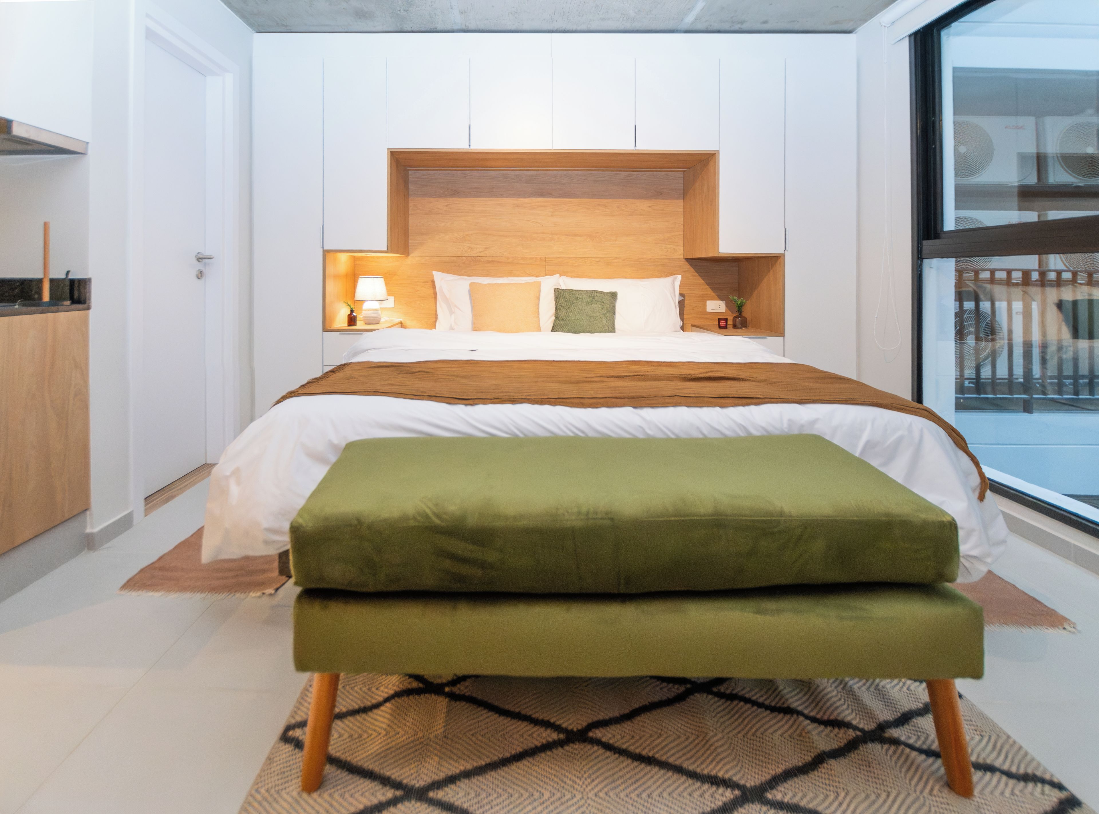 A modern bedroom with a large bed, a wooden headboard, bedside tables with lamps, and a view of the outside through a window.