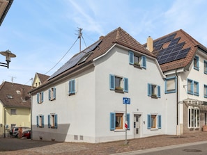 A two-story building with blue shutters, solar panels on the roof, and a clear blue sky.