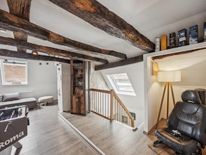 A spacious room with exposed wooden beams, a foosball table, a leather chair, and a bookshelf.