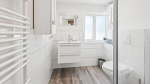 A modern bathroom with a white vanity, a mirror, a window, and a toilet. - Modern group house in the center of Herbolzheim (Herbolzheim)