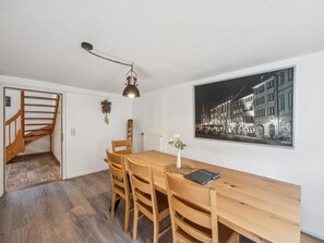 Uma área de refeições com mesa de madeira, cadeiras, luminária pendente, radiador e uma fotografia preto e branco na parede.