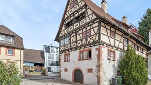A traditional half-timbered house with a steeply pitched roof, a central chimney, and a small front garden. - Modern group house in the center of Herbolzheim (Herbolzheim)