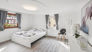 A modern bedroom with a bed, a chair, a radiator, and a window with curtains. - Modern group house in the center of Herbolzheim (Herbolzheim)