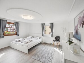 Quarto moderno com cama, cadeira, radiador e janela com cortinas.