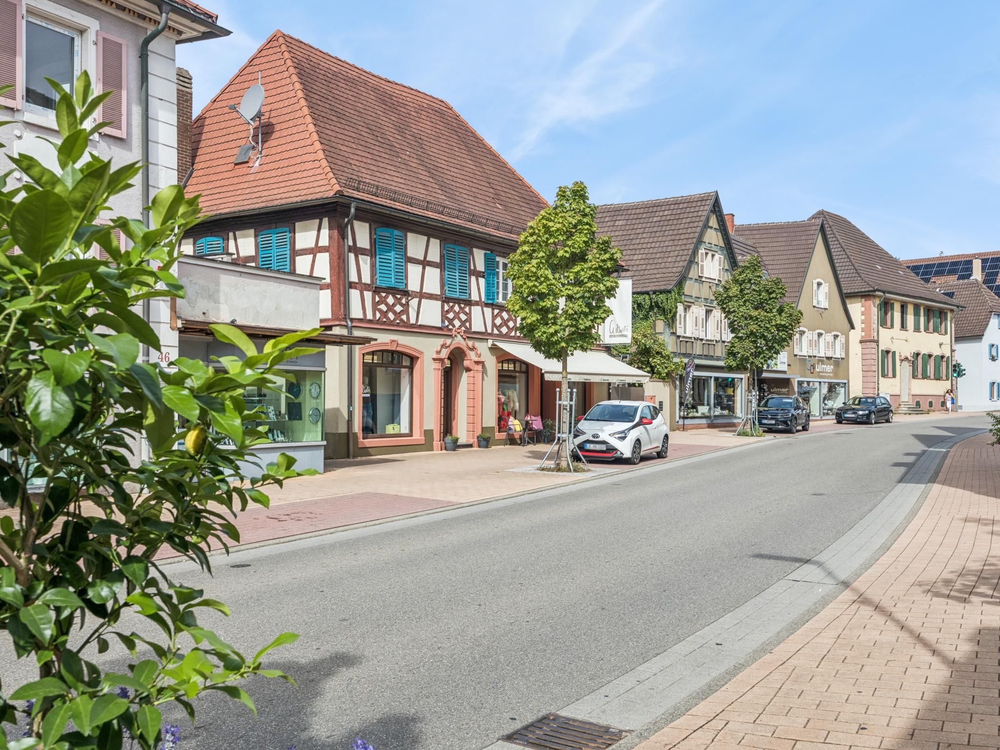A street view with traditional half-timbered houses, a parked car, and a pedestrian walkway.