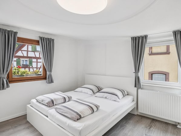 A bedroom with a single bed, a window with curtains, and a radiator.