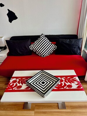 A modern bedroom with a red sofa, black and white striped pillows, a geometric patterned table, and a wall with a black and white design. - Cozy studio with great view in fabulous Waikiki (Honolulu)