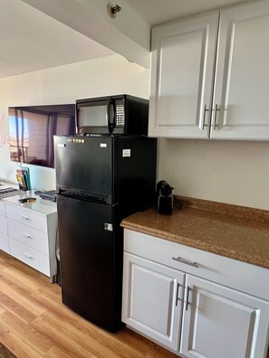A kitchen with white cabinets, a black refrigerator, a microwave, and a coffee maker on the countertop. - Cozy studio with great view in fabulous Waikiki (Honolulu)