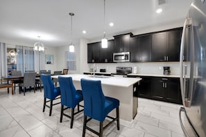 A modern kitchen with dark cabinets, stainless steel appliances, and blue bar stools. - Luxury Villa With Pool And Arcades (Four Corners)