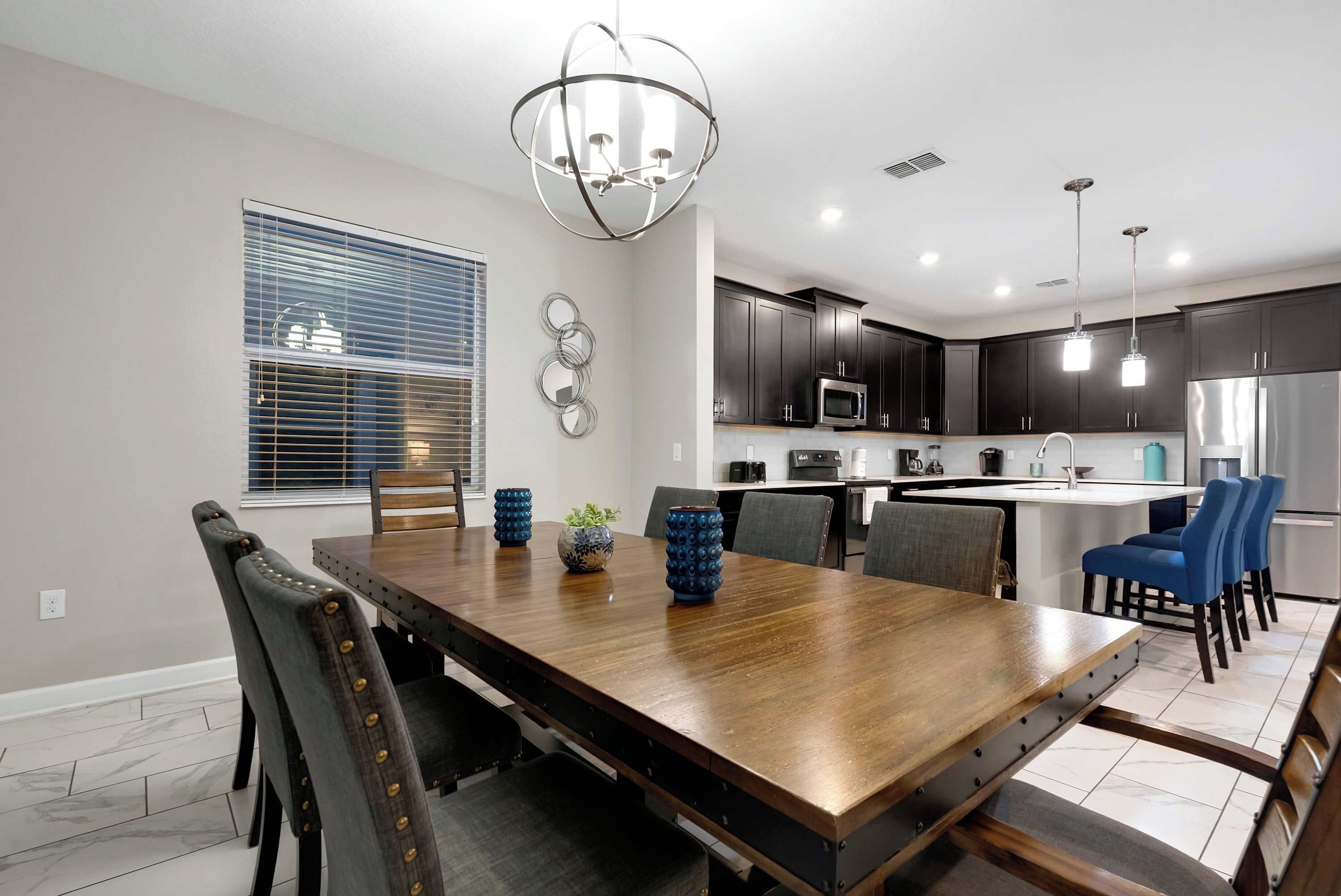 Una cocina moderna con armarios oscuros, electrodomésticos de acero inoxidable y una mesa de comedor de madera con sillas.
