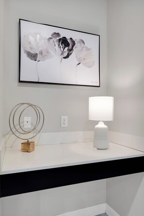 A framed abstract painting on a white wall, a white table lamp on a white countertop, and a metal circular object on the wall. - Luxury Villa With Pool And Arcades (Four Corners)