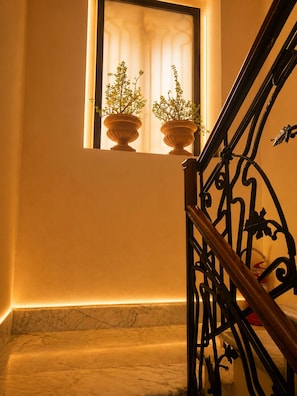 A marble staircase with a wrought iron railing, leading to a window with two potted plants.