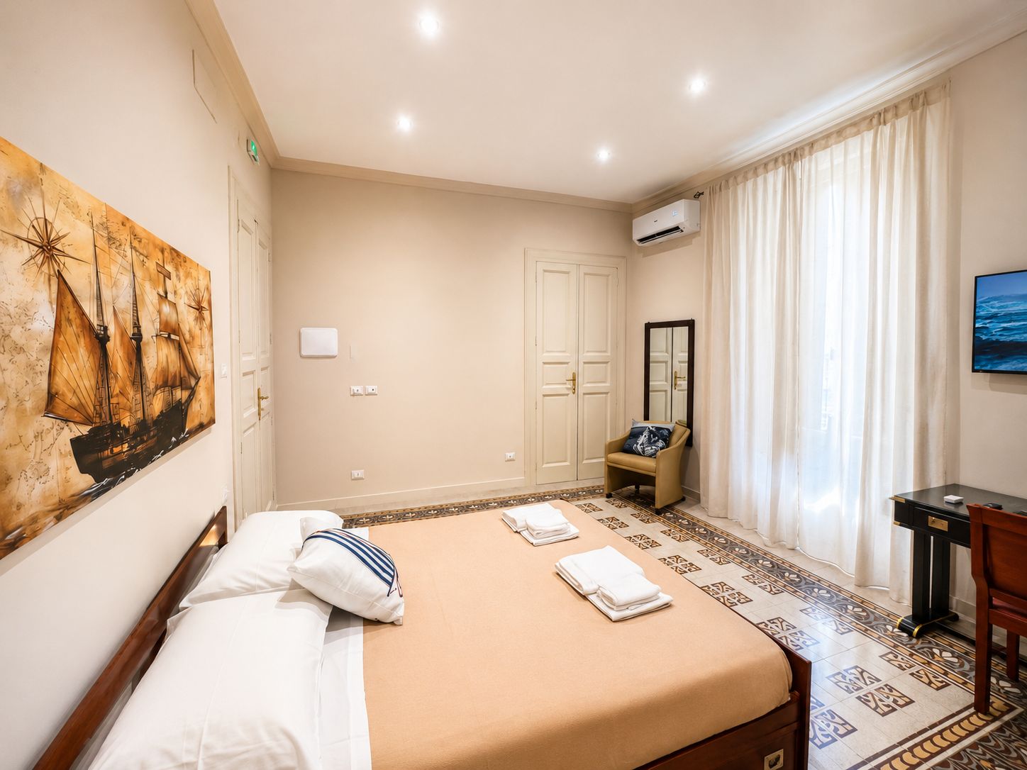 Ein Hotelzimmer mit einem Bett, einem Sessel, einem Schreibtisch, einem Fernseher und einem Bild an der Wand.